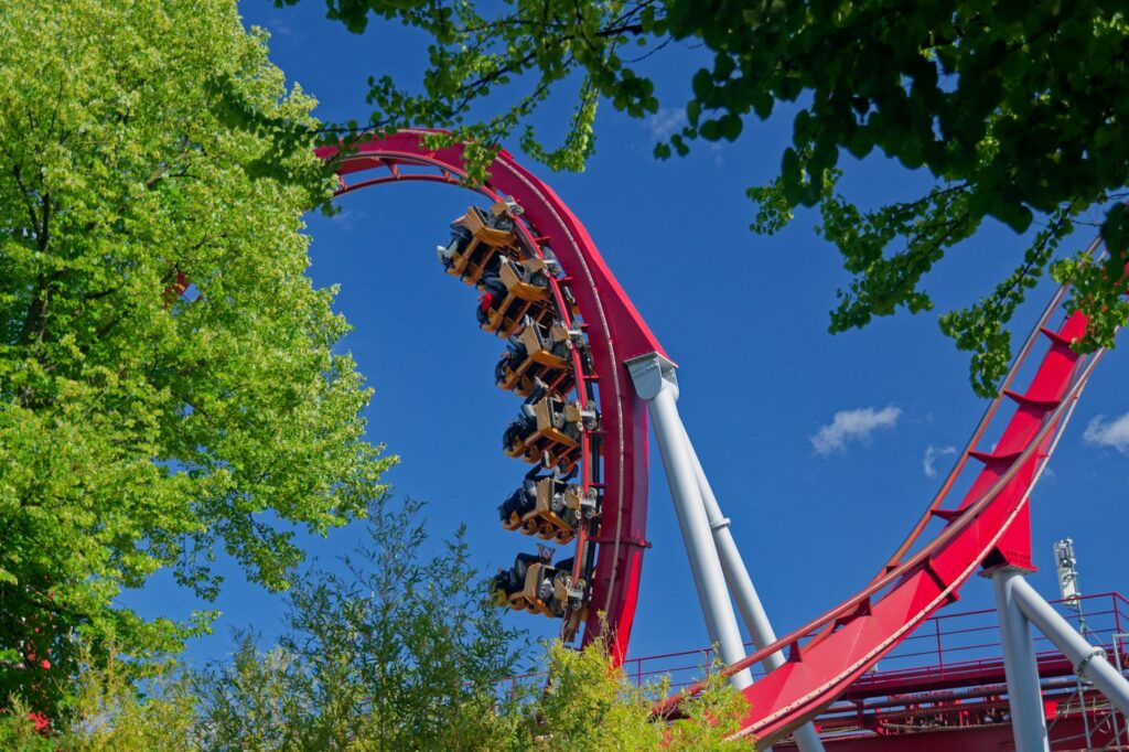 A red roller coaster twisting among green trees